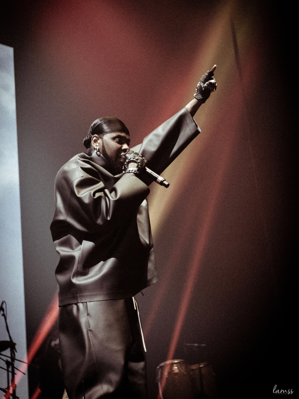 Low-angle shot of Kizz Daniel in a leather-style outfit pointing upwards during a high-energy performance. — concert photography London by Lamss Media